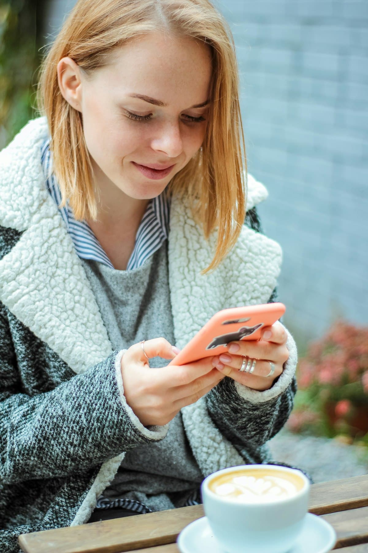 A woman at a café smiling at her phone over a latte