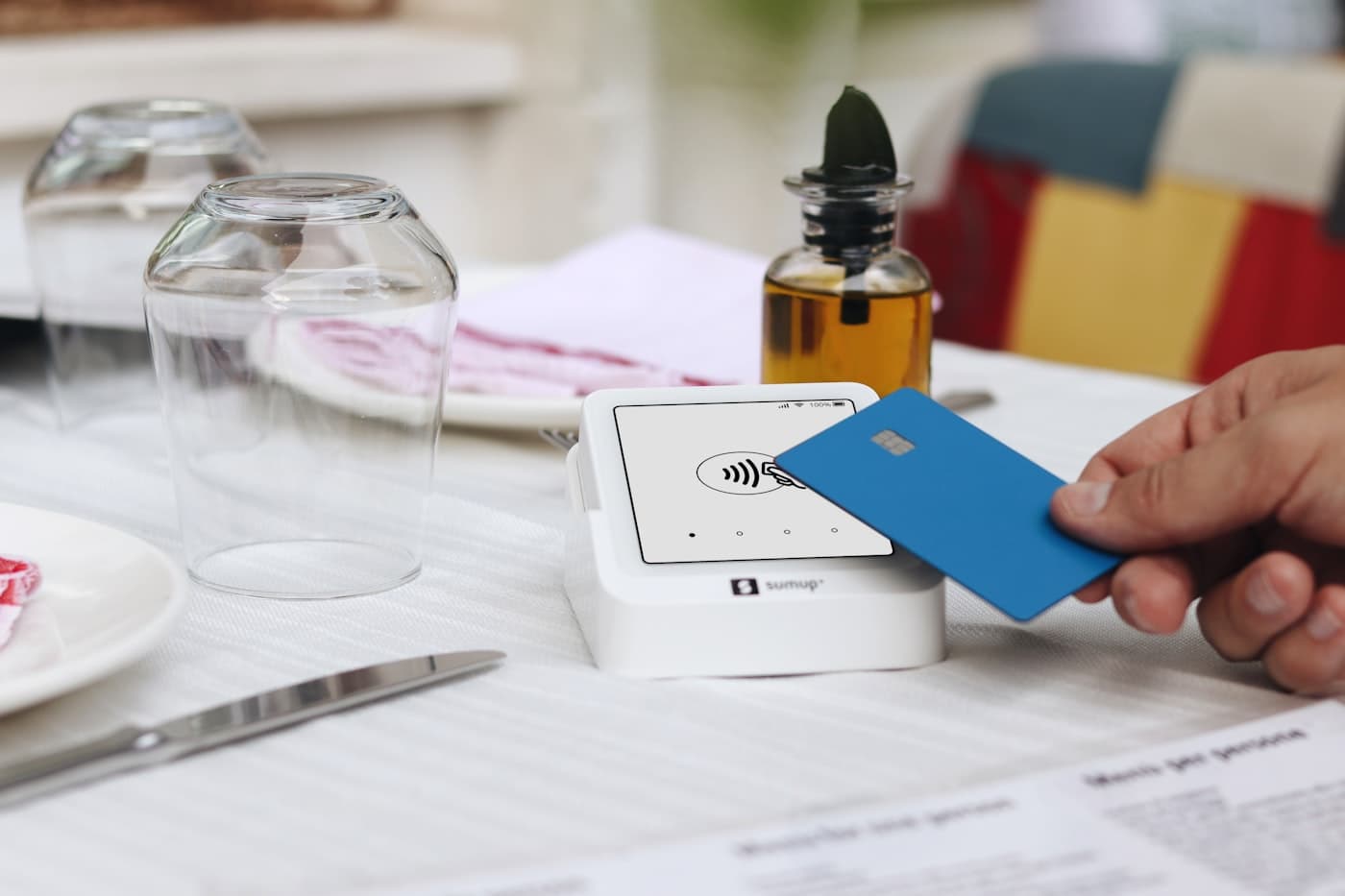 A hand tapping a credit card on a contactless reader at a restaurant table
